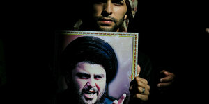Ein mann hält ein Plakat mit einem Foto von Muktada al-Sadr