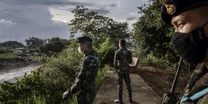 Drei uniformierte Thai-Soldaten mit Gewehren blicken über den Grenzfluß