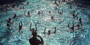 Badende im Schwimmbecken strecken die Arme in die Höhe