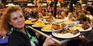 Eine Kellnerin schleppt ein Tablett mit bayrischem Essen