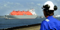 Ein Schiff mit Gasbehältern fährt an einem Hafenarbeiter mit Helm vorbei