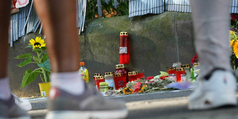 Menschen stehen vor einem Zaun, an dem mit Kerzen und Blumen eines von der Polizei erschossenen Jugendlichen gedacht wird.