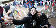 ZWei junge Syrer*innen auf dem Gelände des Landesamts für Soziales in Berlin fotografieren sich lachend mit dem Smartphone