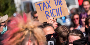 In einer Menge hält jemand ein Schild "Tax the rich" hoch