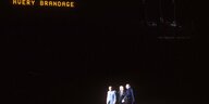 Drei Männer stehen im Lichtkegel bei der Abschlussfeier der Olympischen Spiele 1972. Einer der Männer ist Avery Brundage, auf der Anzeigetafel steht "Thank you Avery Brandage"