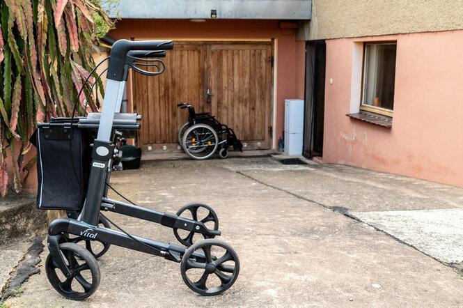 ein Rollaltor steht vor einer Garageneinfahrt, im Hintergrund ein zusammengeklappter Rollstuhl