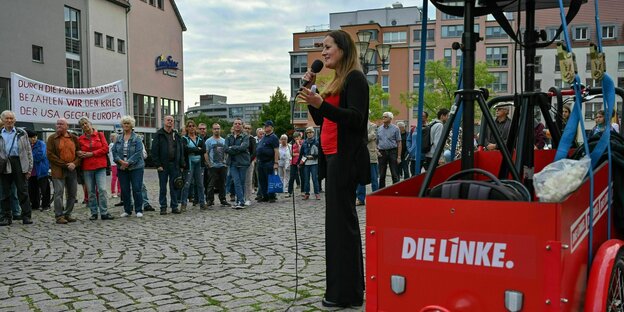 Janine Wissler steht auf einem Platz vor einem roten Lastenrad mit der Aufschrift "Die Linke", umringt von wenigen Menschen