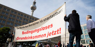 Menschen stehen mit einem Transparent für ein Grundeinkommen auf dem Alexanderplatz