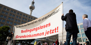 Menschen stehen mit einem Transparent für ein Grundeinkommen auf dem Alexanderplatz