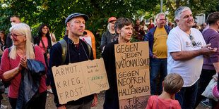 Eine Grupe von Demonstrant:innen, zwei haben sich Protestschilder umgehängt, einer hat ein T-Shirt von Die Basis