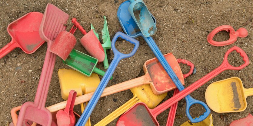 Schaufeln und Eimer liegen auf einem Spielplatz in einem Sandkasten