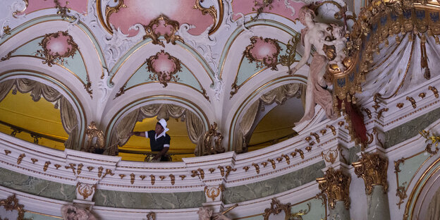 Blick in eine barocke Kuppel, eine Performerin wischt Staub
