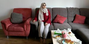 Bayan Alkhatib sitzt auf einem grauen Sofa, sie trägt einen roten Pullover und einen hellen Hijab