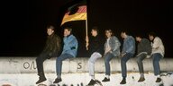 Mehrer Peronen mit Fahne sitzen auf der Berliner Mauer.