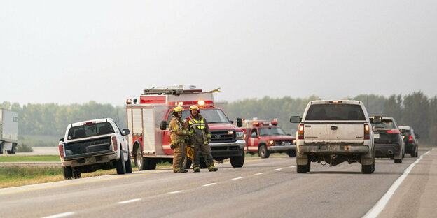 Zei Feuerwehrleute und mehrere Fahrzeuge stehen auf einer Autobahn