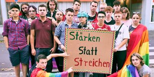 Mit Regenbogenflaggen und dem Plakat "Stärken statt Streichen" protestieren Menschen für anyway e.V.