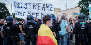 Polizei steht vor einer Menschengruppe die ein Plakat hält worauf "Nordstream 2 sofort öffnen"steht