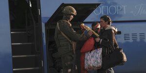 Ein Soldat nimmt einer Frau vor einem Bus Gepäck ab.
