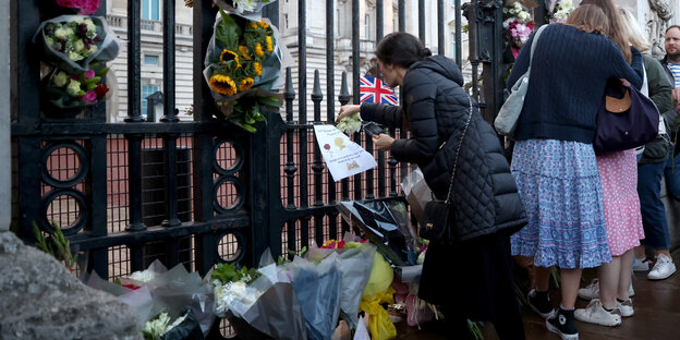 People lay flowers on the fence of Buckinham Palace