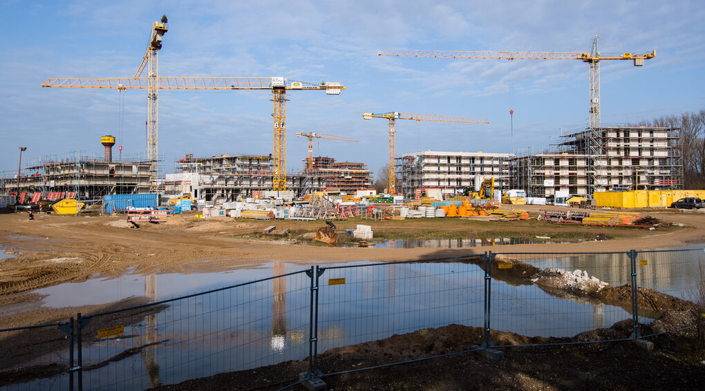 Kräne ragen vor mehreren neugebauten Häuserblocks der Wasserstadt Limmer in Hannover in die Höhe.