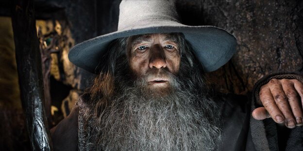 Ein Zauberer mit langem Bart und großen Hut wird von unten angeleuchtet