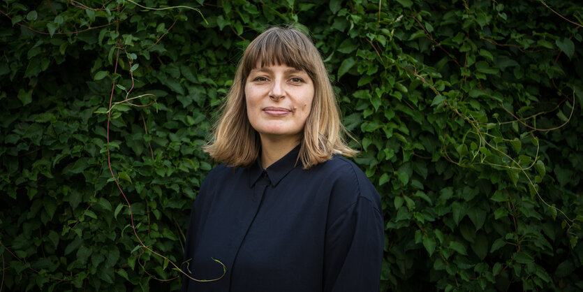 Portrait von Sarah Bäcker vor einer grünen Hecke