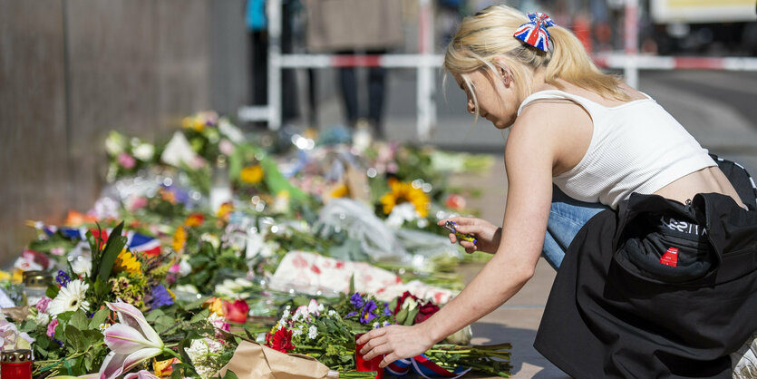 Eine Frau legt Blumen nieder für die Queen