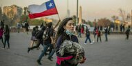 Eine Frau trägt einen Hund über einen Platz, im Hintergrund rennen Menschen mit der chilenischen Flagge