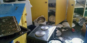 Küche, in der Gegenstände wie eine Mikrowelle durcheinander auf dem Boden liegen. Geschirr fiel aus den Schränken.