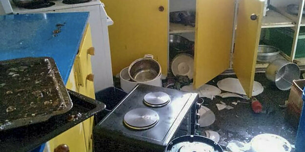 Küche, in der Gegenstände wie eine Mikrowelle durcheinander auf dem Boden liegen. Geschirr fiel aus den Schränken.
