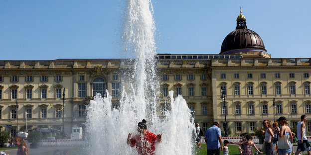 A child plays in a water fountain in front of the Berlin City Palace