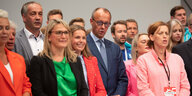 Teilnehmer:innen des CDU-Parteitags singen, in der ersten Reihe stehen Frauen, Merz steht in der zweiten Reihe