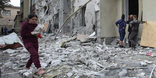 Eine Frau geht mit einem Hündchen in der Hand durch die Trümmer nach einem Raketenangriff