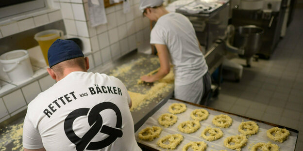 Ein Mann beugt sich über eine Brezelstrasse in der Bäckerei, auf seinem Shirt steht "Rettet uns Bäcker"