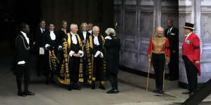 Männer in altmodischen Roben und eine Menschengruppe mit Politikern und Liz Truss im Hintergrund
