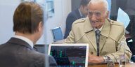 Ein alter Mann im Trenchcoat lässt sich in einer Bank beraten