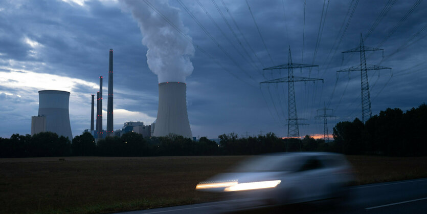 Ein Auto fährt vor dem Uniper-Kraftwerk Staudinger vorbei, im Blick Kühltürme, Schlote und Hochspannungsmasten