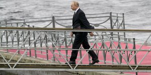 Putin geht über eine Anlegebrücke auf ein Schiff übers Wasser