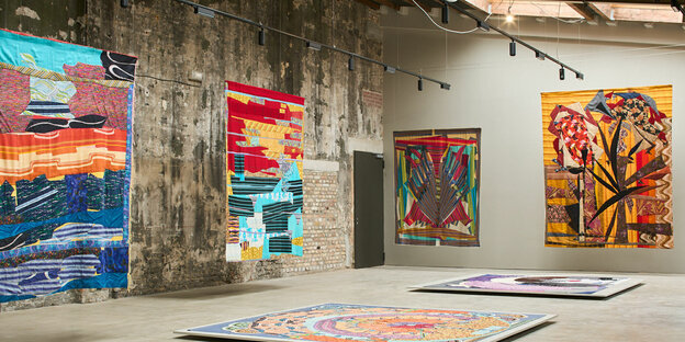 Installationsansicht aus der Gruppenschau „K60“ mit Arbeiten von Noa Eshkol: Bunte, großformatige Arbeiten voller Textilcollagen hängen nahe der Wand von den Decken