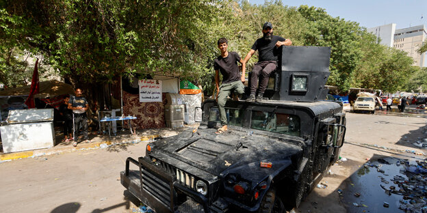 Two men stand on an armored military vehicle