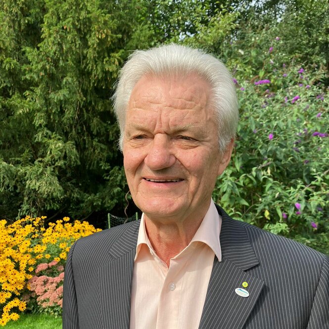 Ein älterer Mann mit weißen Haaren in Jacket und Hemd in einem Garten