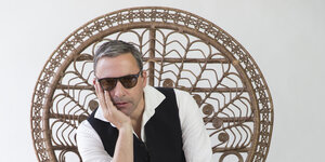 Der Künstler Rocko Schamoni sitzt auf einem Korbsessel und schaut in die Kamera