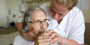 Eine Pflegerin hilft einer 80-jährigen beim Trinken von Wasser