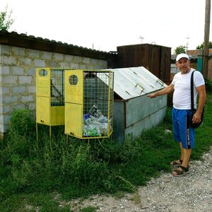 Oleksandr Solotaryov is standing next to a collection bin for plastic bottles on a dirt road in the village