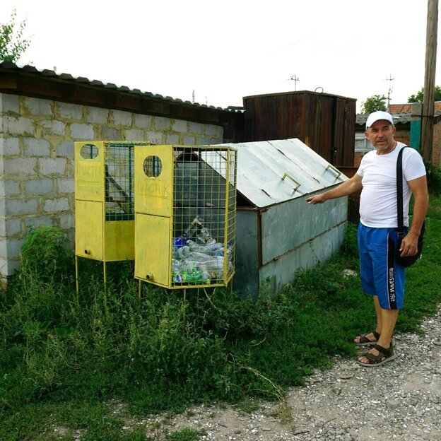 Olexandr Solotarjow steht neben einem Sammelbehälter für Plastikflaschenauf einem unbefestigten Weg im Dorf
