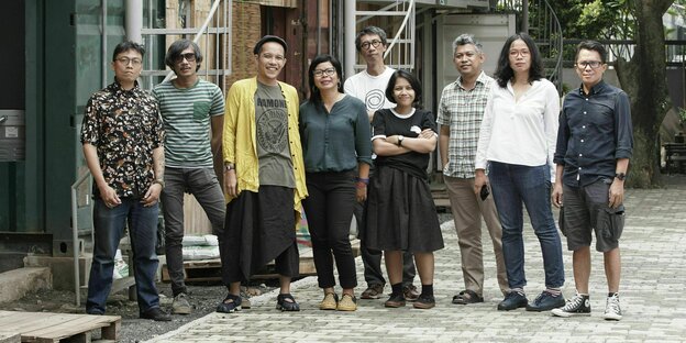 Nine group members from Ruangrupa stand in a courtyard