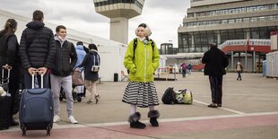 Eine Frau mit neongelber Jacke und Ohrschützern steht vor dem alten Flughafen in Tegel