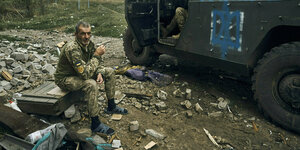 Ein erschöpfter ukrainischer Soldat sitzt vor seinem Jeep und raucht