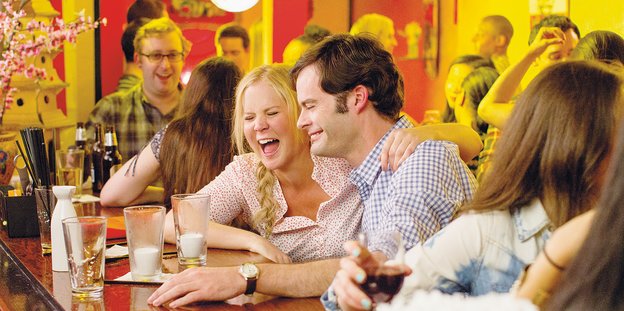 HauptdarstellerInnen Amy Schumer und Bill Hader sitzen an einer Bar und lachen, sie hat einen Arm um seine Schulter gelegt
