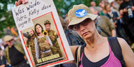 Eine Frau hält ein Schild hoch: "Was würde Petra Kelly dazu sagen?!". Darunter ein Bild des SPIEGEL-Covers "Die Olivgrünen" mit Baerbock, Habeck und Hofreiter.